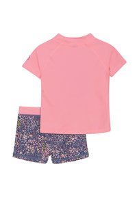 Rash guard i ljusrosa med korta ärmar, matchad med blå shorts med ett blommönster i rosa, gult och vitt.