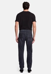 Jeans scuri con vestibilità dritta, caratterizzati da un classico design a cinque tasche e dettagli di cucitura sottili. Indossati con una t-shirt nera.