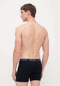 Black boxer shorts made of stretchy fabric, featuring a logoed elastic waistband. Viewed from the back, revealing a fitted design.