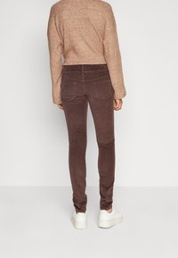 Hnědé kordurové kalhoty slim fit s vysokým pasem a dvěma zadními kapsami, doplněné světlou hnědou pletenou blůzou a bílými teniskami.