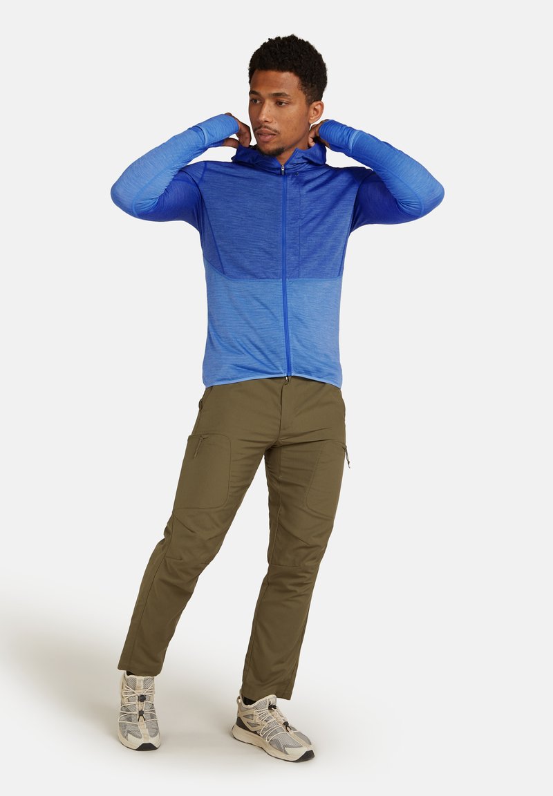 Felpa blu con zip e design degradé, caratterizzata da maniche lunghe e cappuccio. Abbinata a pantaloni cargo oliva e sneakers chiare.