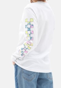 Camisa blanca de manga larga con estampado geométrico multicolor en la manga izquierda en tonos de rosa, amarillo y azul.