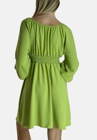 Vestido verde texturizado con una cintura fruncida y mangas largas, que presenta un escote redondeado y una falda fluida que cae por encima de la rodilla.