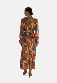 Robe à manches longues en tissu orange avec des motifs de feuilles vertes et crème, taille cintrée et silhouette fluide. Longueur mi-mollet.