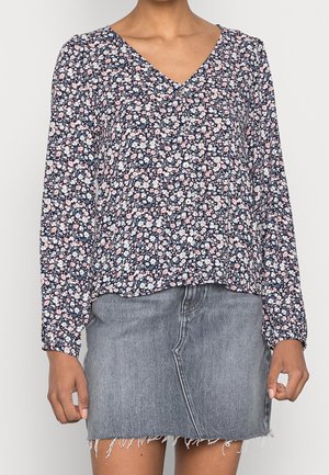 Blouse florale bleu marine à manches longues, décolleté en V, détail de petits boutons, associée à une jupe en denim effilochée. Motif floral en rose et blanc.
