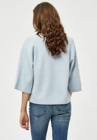 Felpa azzurra chiara, corta, con maniche a 3/4 e un taglio morbido, abbinata a jeans blu scuro con un design classico delle tasche.