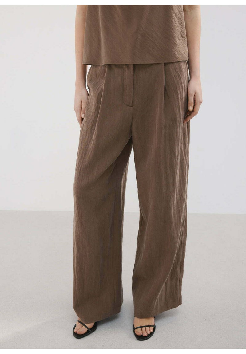 Personne portant un pantalon large en lin marron avec de larges jambes, associé à un haut marron assorti et des sandales noires à bout ouvert.