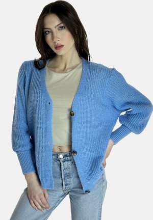 Cardigan de punto azul claro con un patrón texturizado, que presenta un escote en V, tres botones y puños acanalados, llevado sobre una blusa beige.