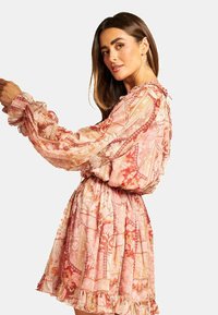 Rosa Blumen-Mini-Kleid mit langen, gepufften Ärmeln, gerüschten Manschetten und tailliertem Design. Durchscheinender Stoff mit filigranen Mustern und Texturen.