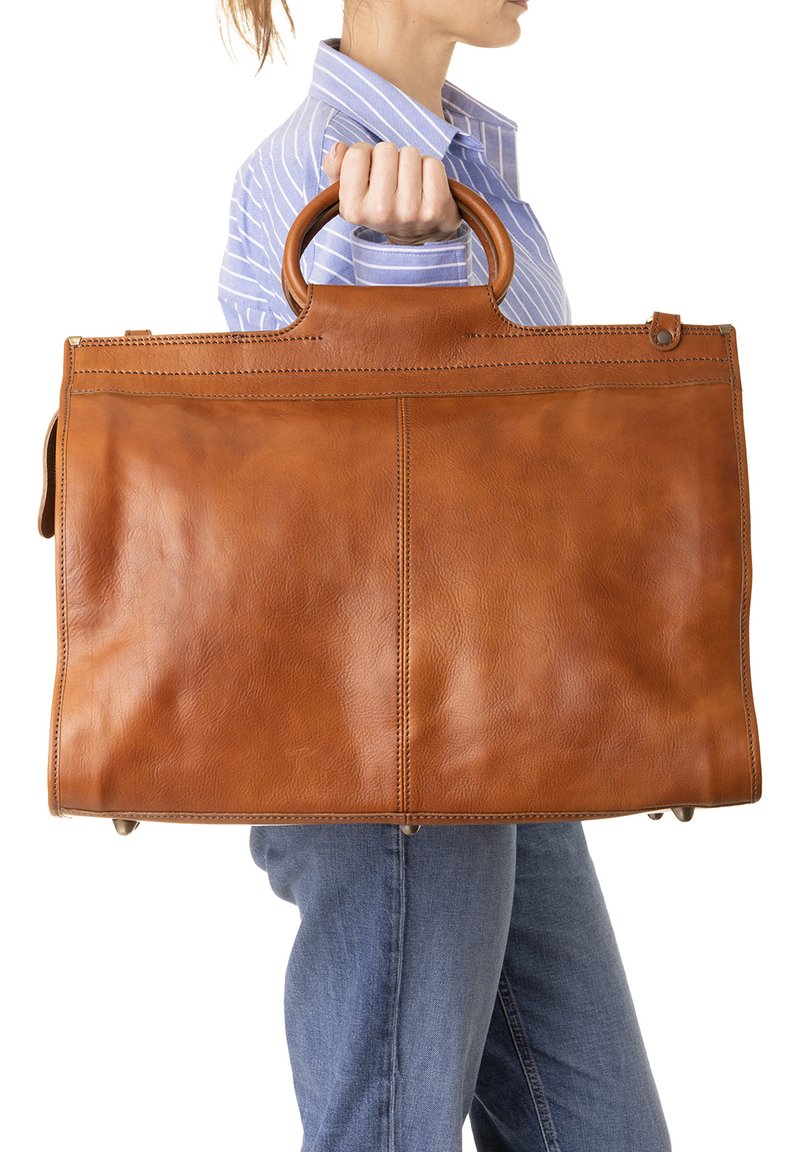 Persona che indossa una camicia a righe blu e jeans, mentre tiene una grande borsa in pelle marrone con manici rotondi ai lati.