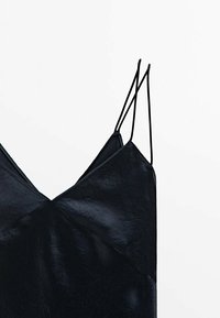 Robe noire sans manches avec un col en V, en tissu brillant et texturé. Dispose de fines bretelles ajustables et d'un détail décoratif en couture.