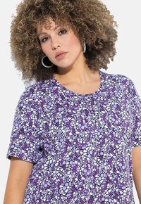 Top corto viola a maniche corte con un motivo floreale e geometrico in bianco e nero. Collo rotondo, vestibilità rilassata e texture del tessuto liscia.