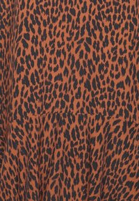 Látka s leopardím potiskem v oranžové a černé barvě, s měkkou strukturou a různými velikostmi skvrn na materiálu, vytvářející dynamický vzor.