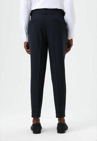 Marineblauwe, op maat gemaakte broek met een gladde textuur, voorzien van twee achterzakken en een taps toelopend ontwerp, omgeslagen bij de enkels.