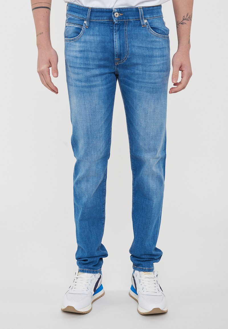 Jeans in denim azzurro chiaro con vestibilità slim, con cuciture a contrasto, cinque tasche e chiusura con bottone. Modello che indossa sneakers bianche.