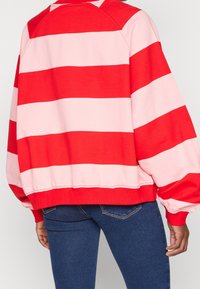 Felpa a righe rossa e rosa con collo rotondo, vestibilità ampia e polsini a costine. Indossata con jeans blu scuro, dotati di tasche posteriori.