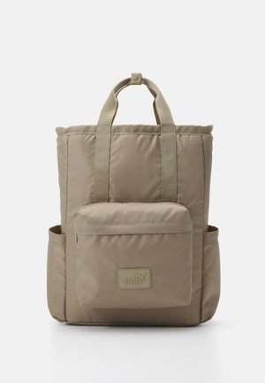 Mochila beige de Puma con bolsillo delantero con cremallera, dos bolsillos laterales y asas superiores para llevar, sobre un fondo blanco.