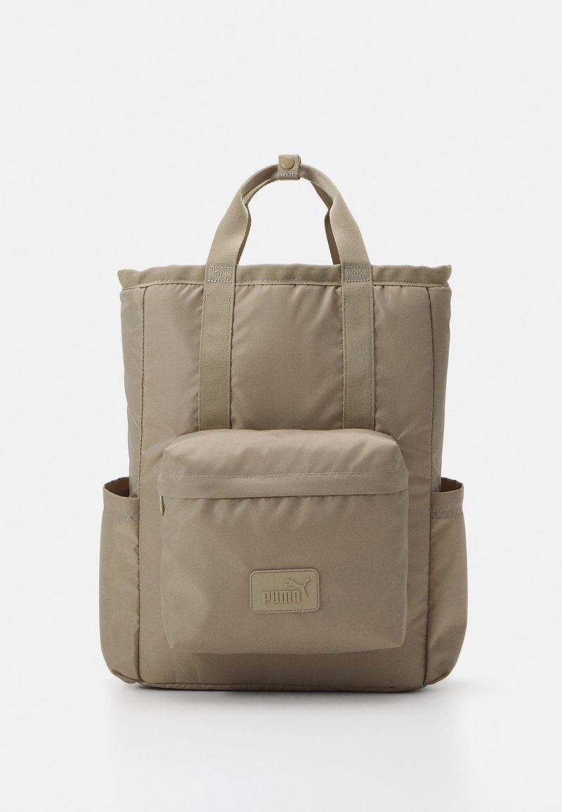 Sac à dos beige Puma avec poche avant zippée, deux poches latérales et poignées supérieures sur fond blanc.