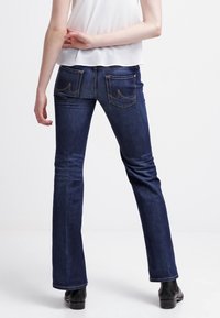 Jeans acampanados de denim azul oscuro con una cintura ajustada y bolsillos traseros con costura curva. La tela tiene una textura suave y ligeramente elástica.