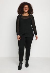 Black long-sleeve top with a textured mesh design, featuring a scoop neckline. Paired with fitted black jeans and ankle boots.