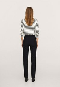 Chemise à rayures à manches longues blanche et marine, associée à un pantalon noir ajusté. Présente une taille haute et une silhouette ajustée, avec une texture de tissu lisse.