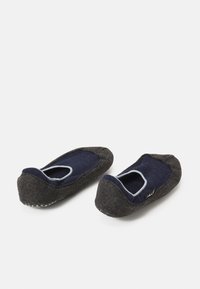 Chaussons en feutre gris avec une doublure en tissu bleu marine, forme de orteil arrondie, ouverture élastique et semelle texturée pour une meilleure adhérence.