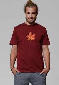 Bordeaux t-shirt met een geometrische oranje esdoornbladprint op de voorkant. Korte mouwen en ronde halslijn, vervaardigd uit zachte materialen.