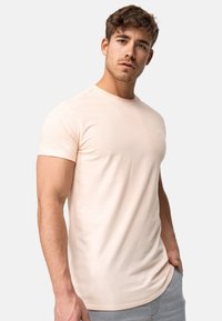 Helles rosa T-Shirt mit kurzen Ärmeln aus weichem Stoff und Rundhalsausschnitt. Verfügt über ein kleines Emblem auf der Brust und einen geschwungenen Saum.