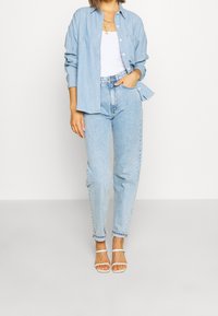 Jasnoniebieska koszula chambray, biała bluzka na ramiączkach, jasnoniebieskie dżinsy prostego kroju i białe sandały na ramiączkach. Miękka tkanina, luźny krój, swobodny wygląd.