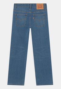Blue denim jeans with a straight leg design, visible stitching, two back pockets, and a branded leather patch at the waist.