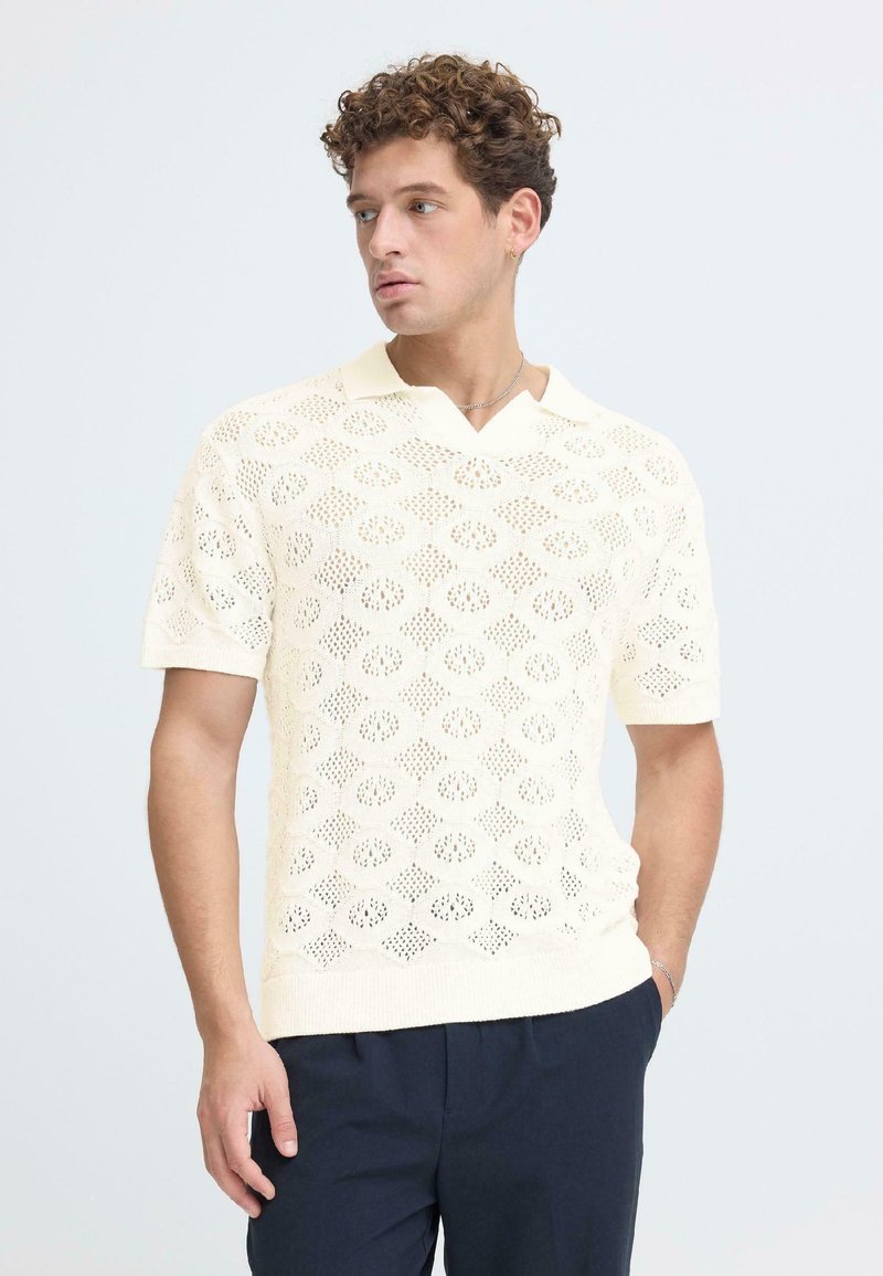 Gestrickter Kurzarm-Pullover in hellem Creme mit offenem Diamantmuster, V-Ausschnitt und lockerem Schnitt. Weiche Textur.