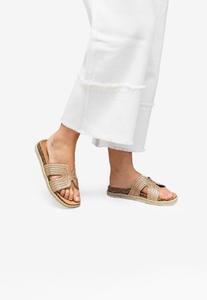 Sandales à glissière tressées beige avec un design de bride courbée, semelle en fibre naturelle et dessus texturé. Portées avec un pantalon blanc à ourlet effiloché.