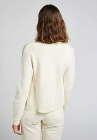 Pull crème, à côtes, avec une coupe décontractée, doté d'un col arrondi et de manches tombantes, confectionné en tissu doux et texturé.