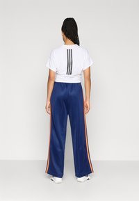 Hvit croppet t-skjorte med tre svarte vertikale striper på baksiden, kombinert med blå bukser med oransje sidestriper og en løs passform.