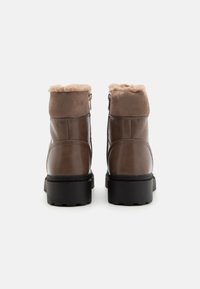 Bottines en cuir marron avec doublure en peluche beige, fermeture éclair sur le côté et talon anglé. Dotées d'une semelle en caoutchouc noir texturé pour une traction optimale.