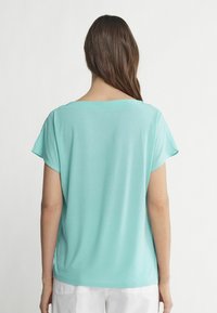 Ljus turkos kortärmad topp med bred halsringning och avslappnad passform. Slät textur, enkelt mönster och inga framträdande mönster eller accenter.