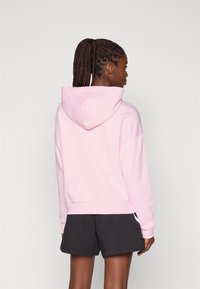 Sweat-shirt à capuche rose avec une coupe décontractée, ourlet et poignets côtelés, associé à un short noir. Le tissu semble doux et lisse.
