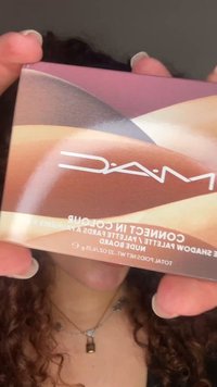 Hands holding a MAC eyeshadow palette with abstract wavy shades of pink, brown, beige, and gray.