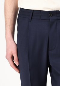 Granatowe dopasowane spodnie wykonane z lekkiego materiału, z płaskim przodem, bocznymi kieszeniami i zapięciem na pojedynczy guzik.