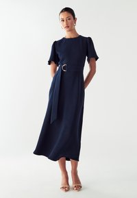 Námorníckomodrá šaty s krátkymi puff rukávmi, priliehavým telom a opaskom s zlatou sponou. Hladká tkanina, dĺžka po členky a minimalistický dizajn.