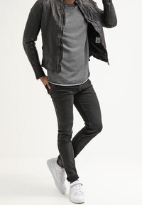 Giacca nera in pelle con zip, maglione grigio a girocollo, jeans neri slim-fit e sneaker bianche. Texture lisce con accenti minimali.