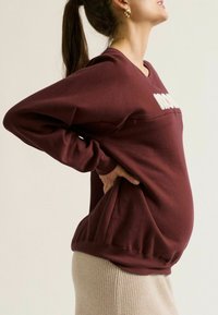 Bordeaux sweatshirt met gestructureerde letters, relaxed fit en geribbelde zoom. Gecombineerd met een lichte, geribbelde rok, die een rond buikje laat zien.