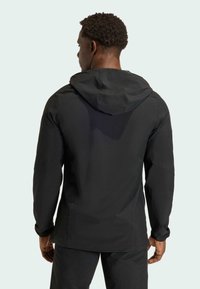 Chaqueta negra con capucha de textura suave, con mangas largas, silueta ajustada y sutiles detalles de costura en la parte posterior.