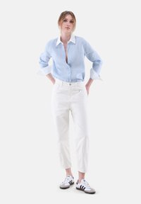 Light blue striped button-up shirt with white collar and cuffs, paired with white high-waisted jeans and black and white sneakers.