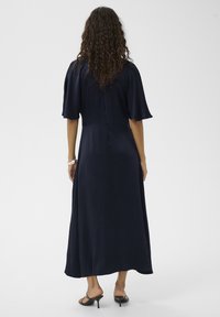 Temno modra maxi obleka s kratkimi rožnatimi rokavi, oprijetim zgornjim delom in tekočo krilom. Gladek tekstura, zračen material.