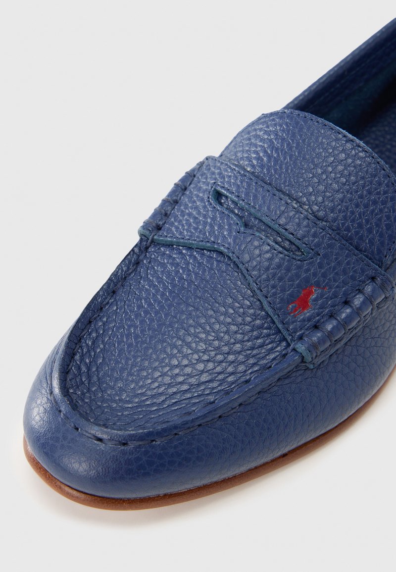 Mocassino in pelle blu con finitura testurizzata, cuciture dettagliate e piccolo emblema rosso. Punta arrotondata e morbida fodera interna.