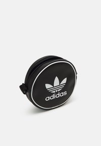 Borsa rotonda nera Adidas con rifiniture bianche, chiusura con zip e logo trefoil Adidas sul davanti, su uno sfondo bianco uniforme.