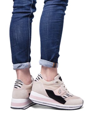 Zapatillas beige y negras con un upper texturizado, parte trasera a rayas, suela blanca y acento rosa, con detalle del logo en el lateral.
