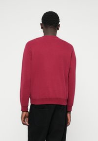 Sweatshirt bordeaux avec un col rond, des poignets et un ourlet côtelés. La vue arrière montre une texture lisse et un design simple sans graphique.