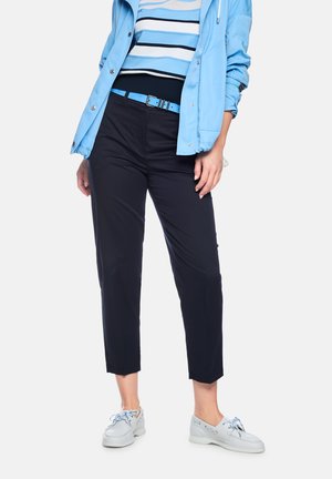 Woman wearing black cropped pants, light blue belt, striped blue sweater, light blue jacket, and light gray shoes with blue laces.